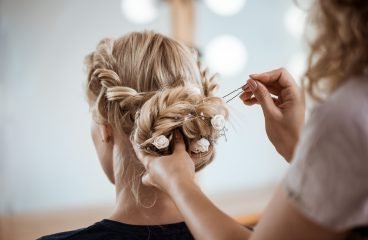 Female hairdresser making hairstyle to beautiful blonde girl in beauty salon. Copy space.